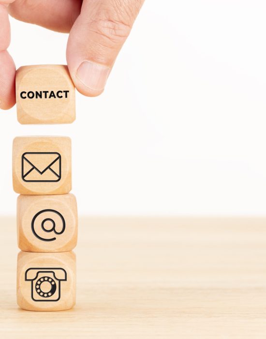 Contact us concept. Hand holding a wooden block with text and a pile of dices with communication icon. Copy space