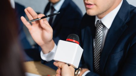 partial view of journalist with microphone interviewing politician during party congress on blurred