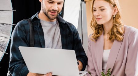 smiling young photographer and female model using laptop in photo studio